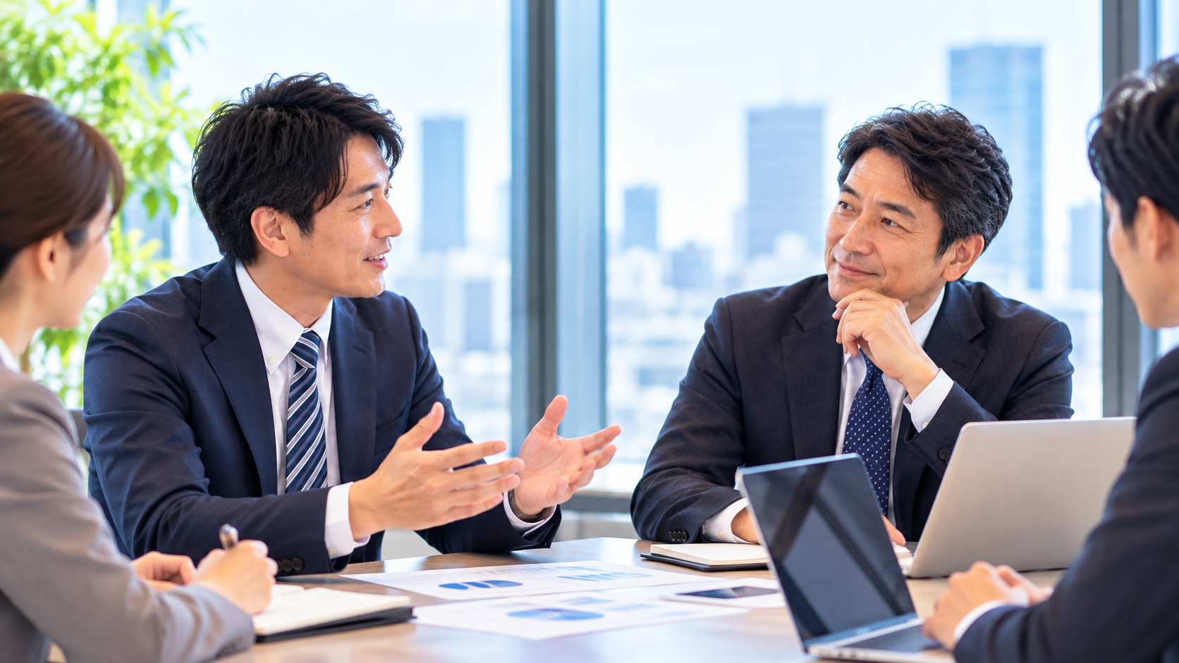 会議室で部長が報告し、経営者と出席者が耳を傾けている様子